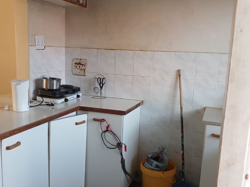 A compact kitchen featuring tiled splashbacks, laminate countertops, and built-in cabinetry, currently requiring maintenance and cosmetic updates to improve functionality and aesthetic appeal.