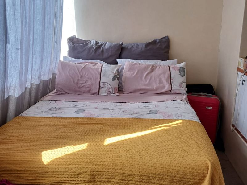 A compact bedroom featuring a large window with curtains, providing natural light to the sleeping area.