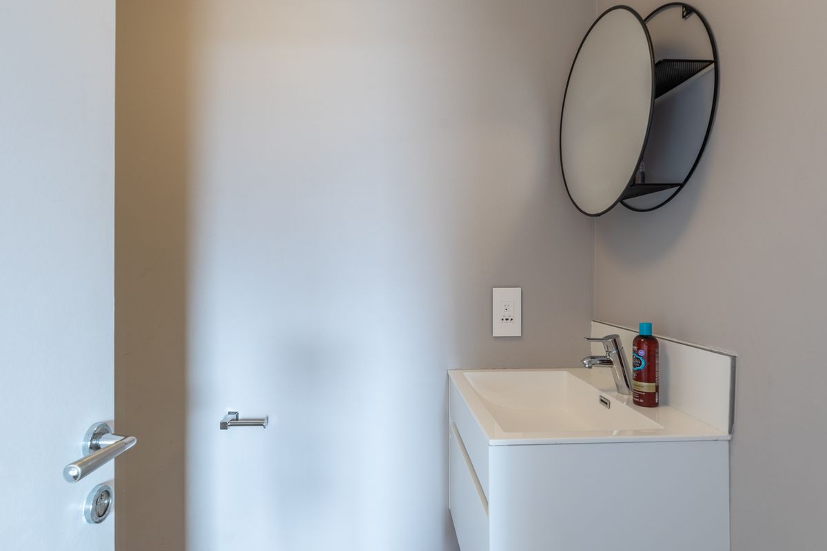 A clean and modern bathroom featuring a wall-mounted vanity with an integrated basin, chrome mixer tap, and a circular wall mirror.