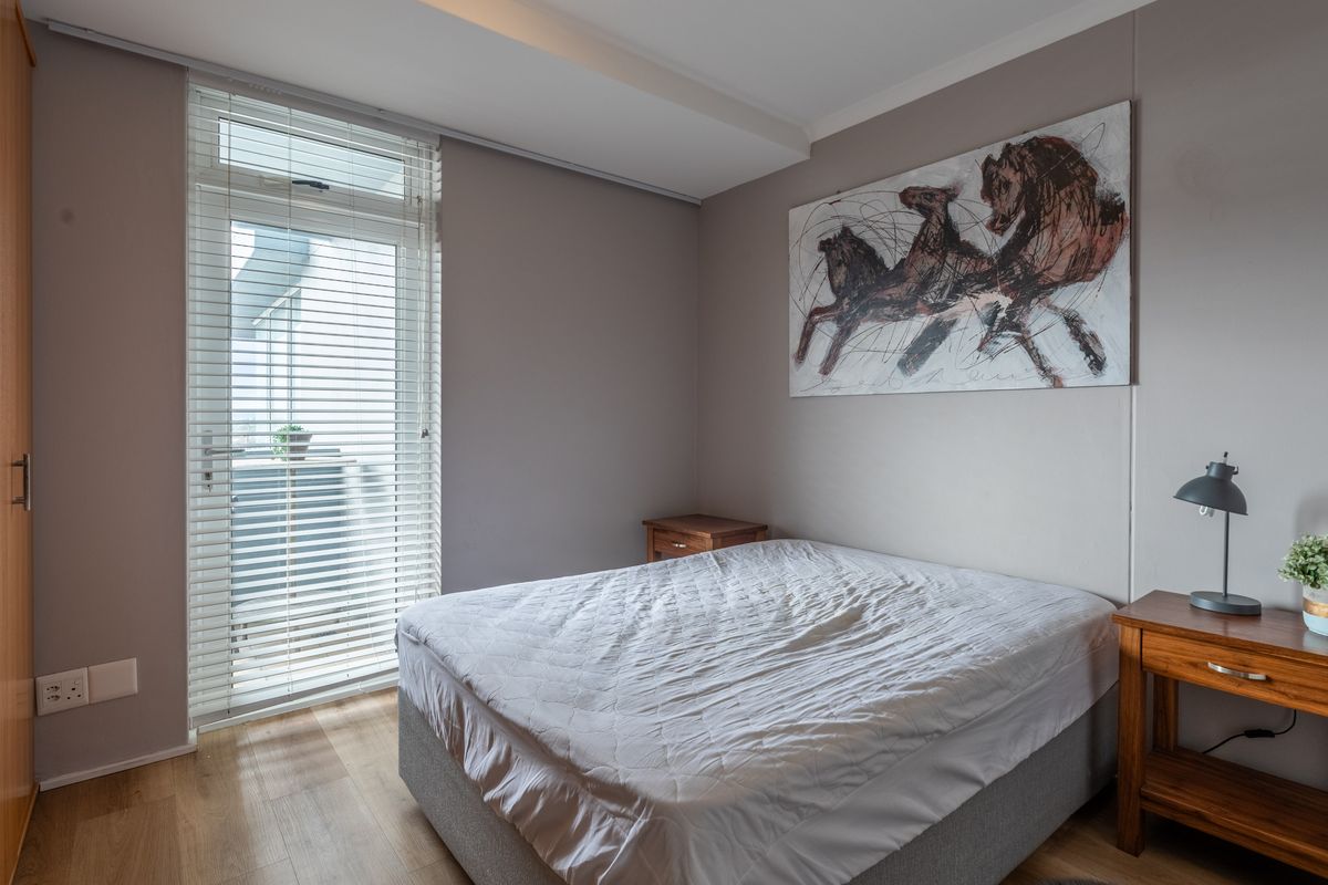 A well-maintained bedroom featuring laminate flooring, a built-in wardrobe, and a glass door with venetian blinds providing access to an outdoor area.