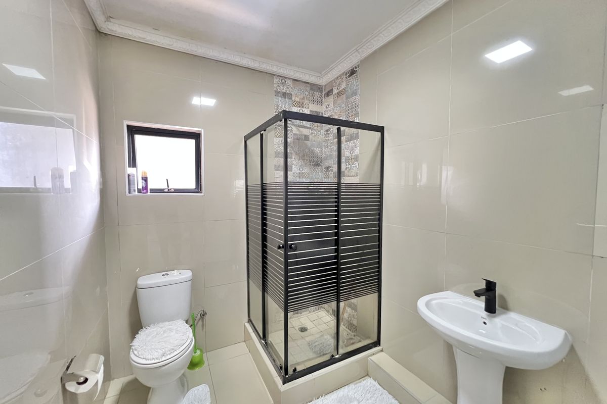 Modern bathroom featuring a corner shower enclosure with black frame, pedestal basin, and neutral wall tiling.