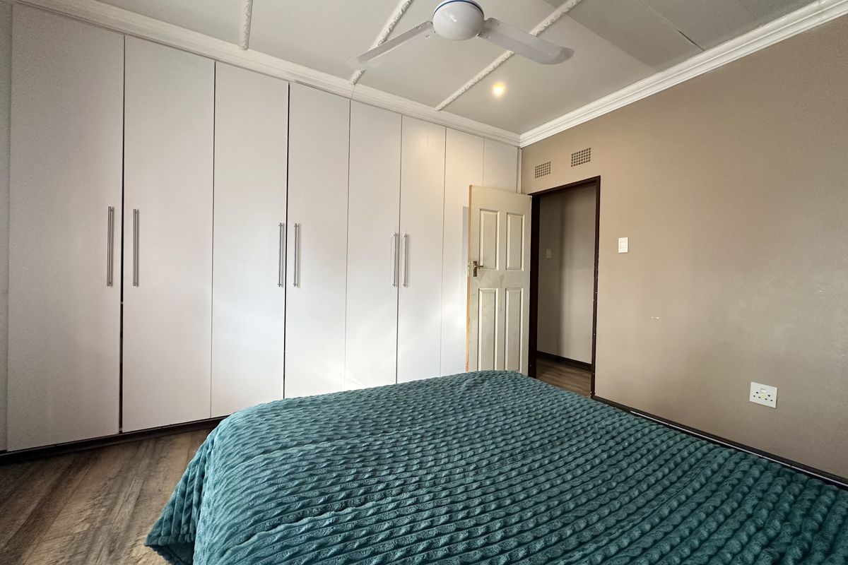 A bedroom featuring extensive white built-in cupboards, a ceiling fan, and laminate flooring, offering a functional and neutral living space.