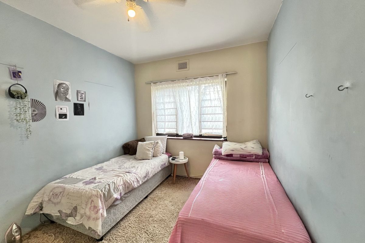 A bedroom featuring a ceiling fan, louvered window, and wall vent, with carpet flooring and light blue wall finishes.
