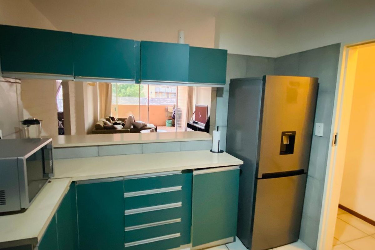 A functional kitchen featuring teal cabinetry, laminate countertops, and tiled backsplash, with an open-plan layout overlooking the living area.