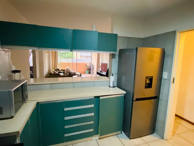 A functional kitchen featuring teal cabinetry, laminate countertops, and tiled backsplash, with an open-plan layout overlooking the living area.
