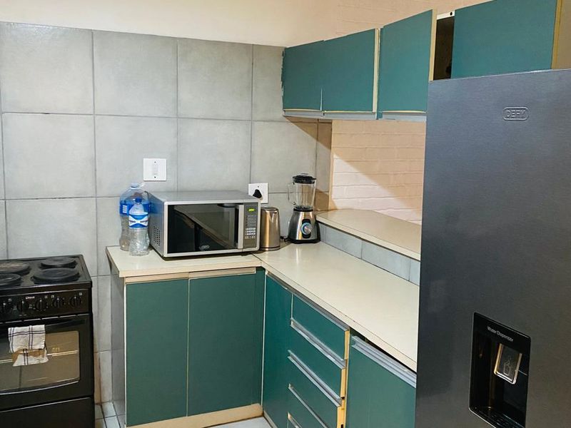 A functional kitchen featuring green cabinetry, tiled backsplash, and tiled flooring, currently showing signs of wear and requiring cosmetic updates.
