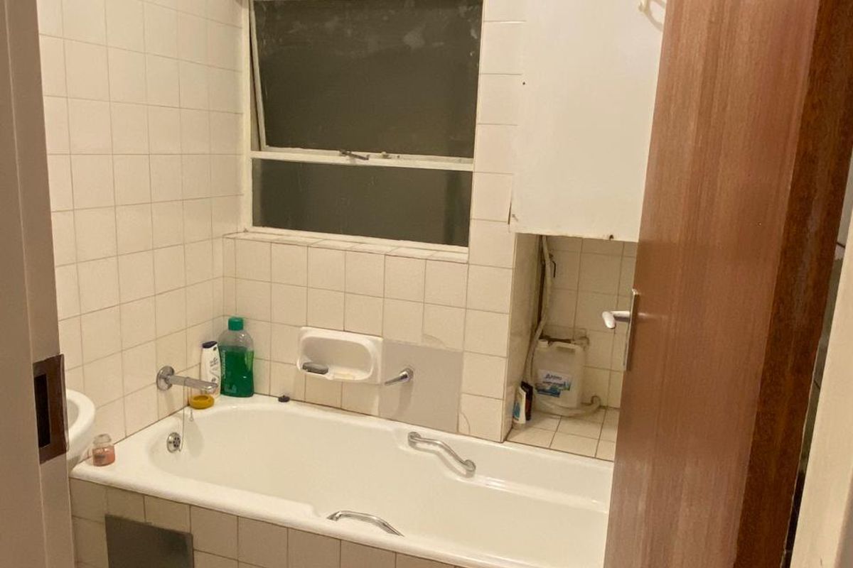 A dated bathroom featuring a built-in bathtub, tiled walls and flooring, and integrated cabinetry, requiring cosmetic updates to improve its overall condition and appeal.