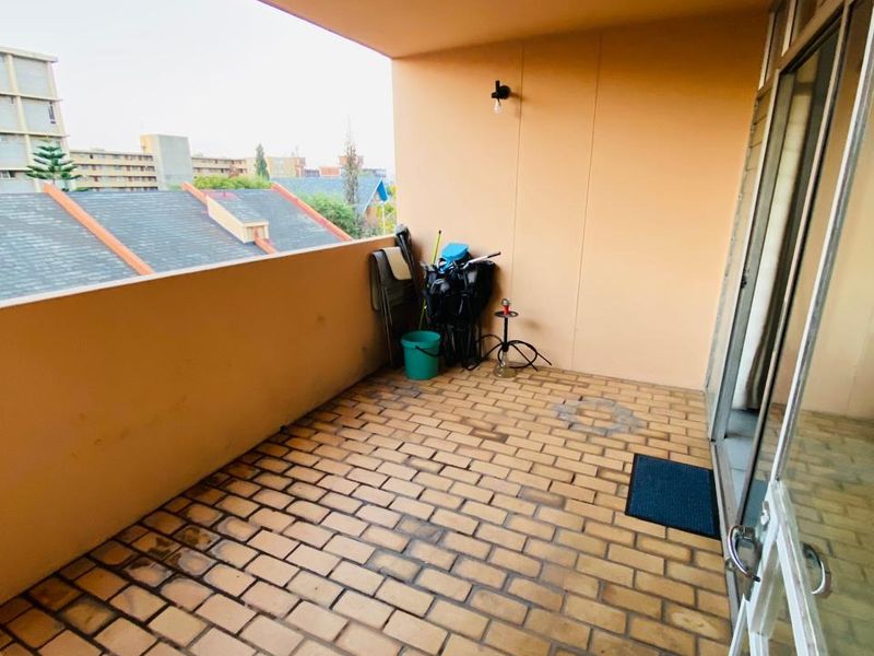 A covered balcony featuring brick flooring, a wall-mounted light, and access via a sliding glass door, offering an open-air space for relaxation.