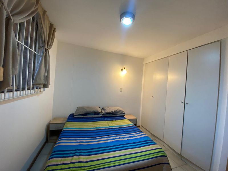 A functional bedroom featuring built-in cupboards, tiled flooring, and security bars on the window, providing a practical and secure living space.