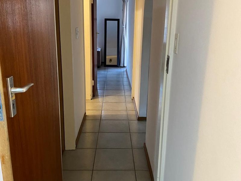 A functional hallway featuring neutral tiled flooring and an arched transition, providing access to adjacent rooms within the apartment.