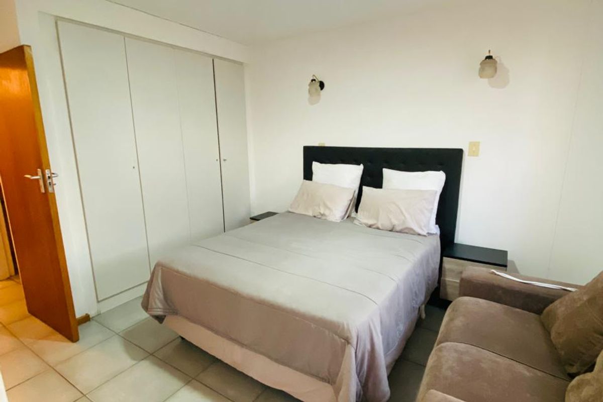 A functional bedroom featuring tiled flooring, built-in cupboards, and wall-mounted lighting, providing a practical and neutral living space.