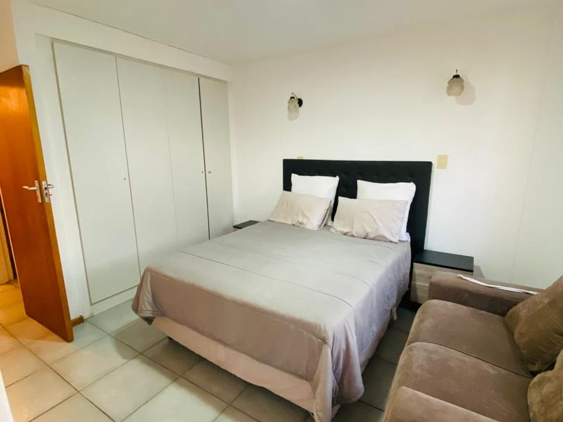 A functional bedroom featuring tiled flooring, built-in cupboards, and wall-mounted lighting, providing a practical and neutral living space.
