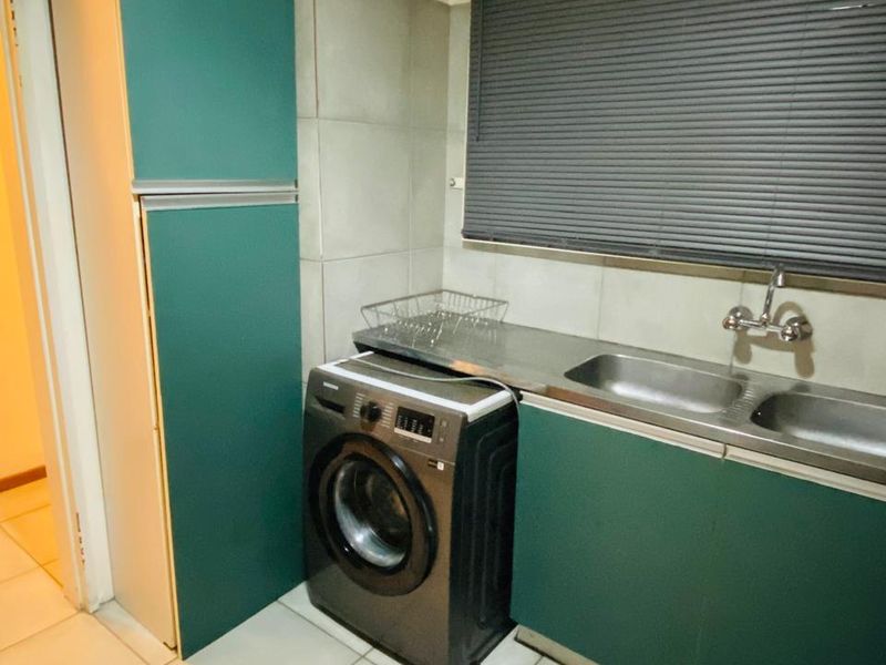 A functional laundry area featuring built-in green cabinetry, a stainless steel double sink, tiled backsplash, and tiled flooring.