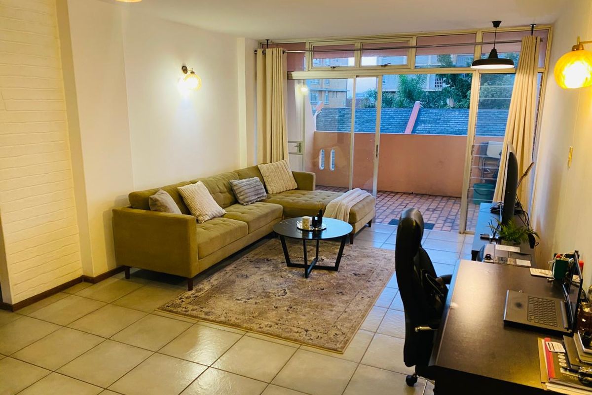 A well-lit living room featuring tiled flooring, a textured feature wall, and large sliding glass doors providing access to an outdoor balcony area.