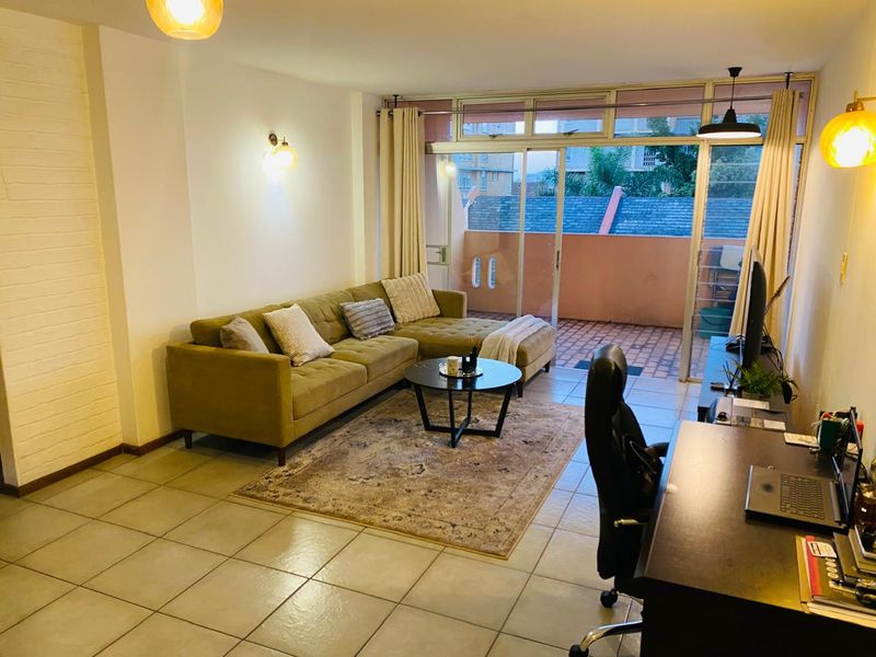 A well-lit living room featuring tiled flooring, a textured feature wall, and large sliding glass doors providing access to an outdoor balcony area.