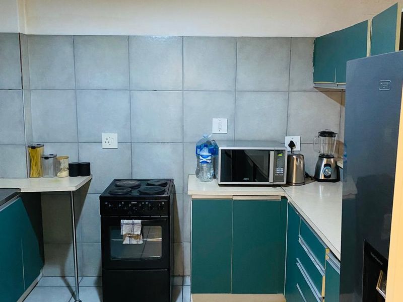 A functional kitchen featuring teal cabinetry, tiled backsplash, and tiled flooring, equipped with a freestanding stove and built-in microwave space.