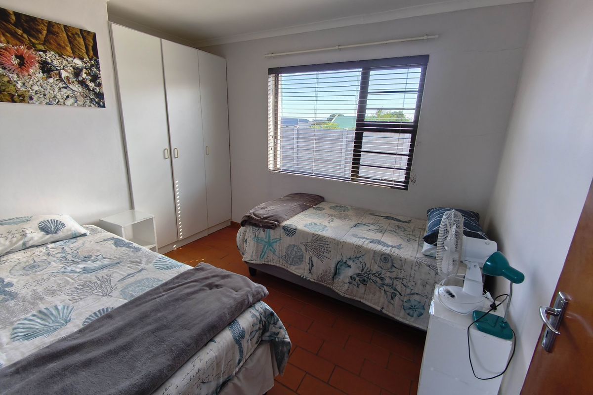 A functional bedroom featuring built-in wardrobes, tiled flooring, and a window with horizontal blinds, offering a simple and practical living space.