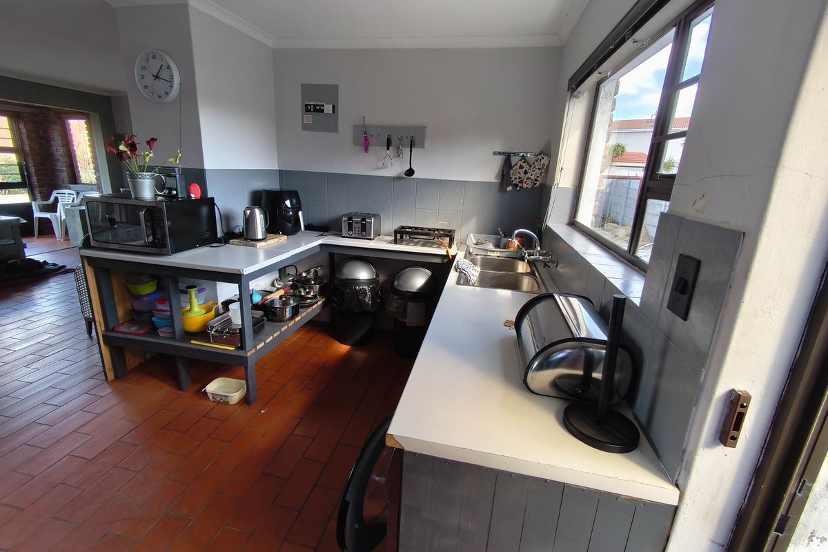 A functional kitchen area featuring terracotta flooring, double stainless steel sink, tiled splashbacks, and ample counter space with a view to the exterior.