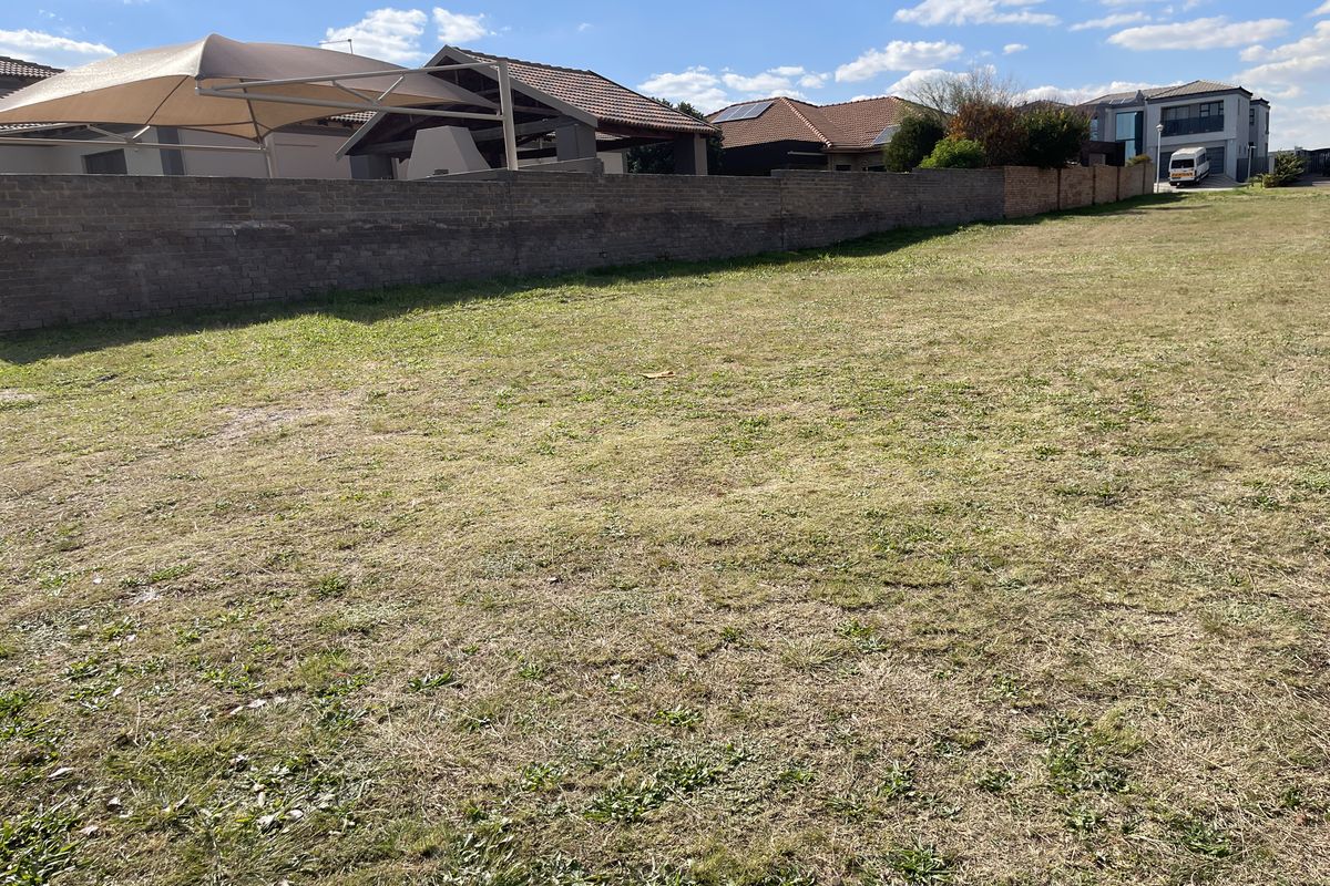 A vacant residential plot featuring a grass lawn and a perimeter boundary wall, situated in a developed suburban neighborhood.