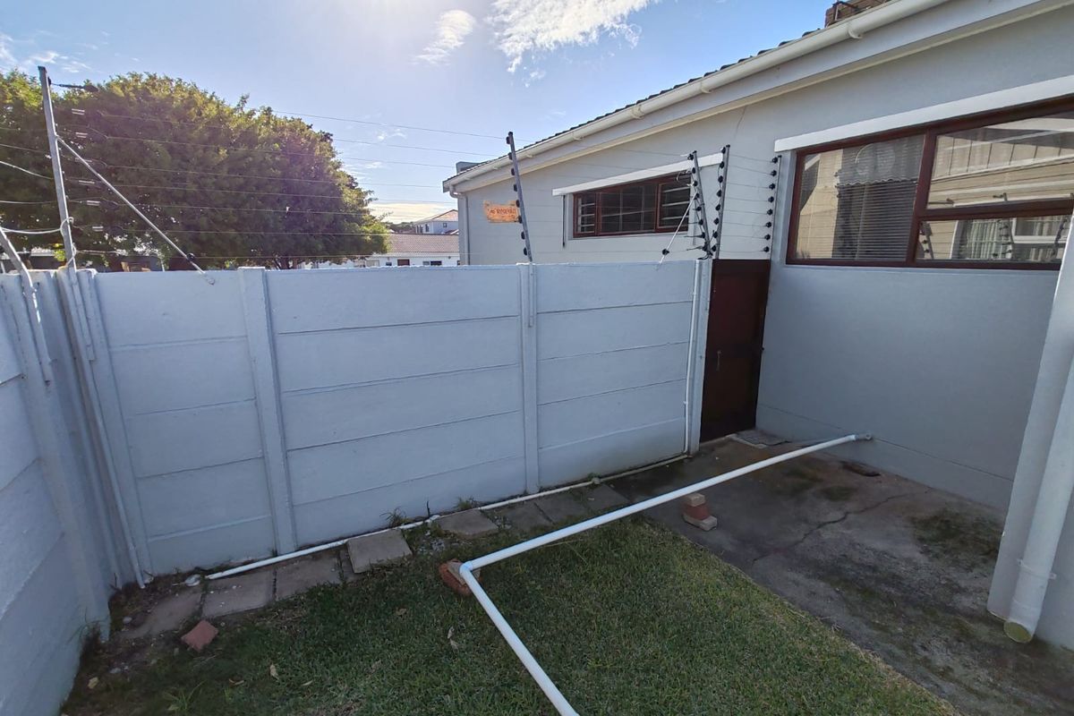 A rear exterior view of the property featuring a precast concrete boundary wall with electric fencing and a small paved section.