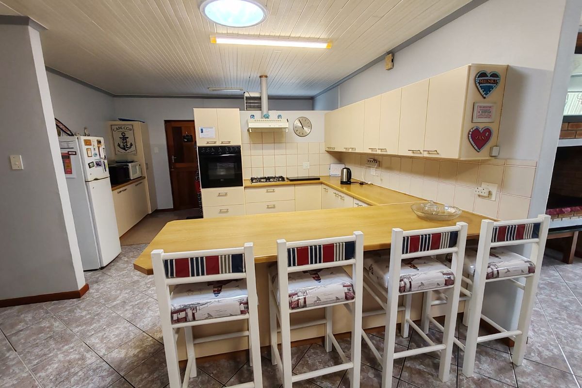 A functional kitchen featuring light-toned cabinetry, a breakfast bar, built-in oven, gas hob, and tiled flooring, illuminated by a central skylight.