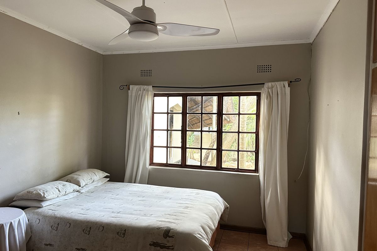 A functional bedroom featuring tiled flooring, a ceiling fan, and a timber-framed window with natural light.