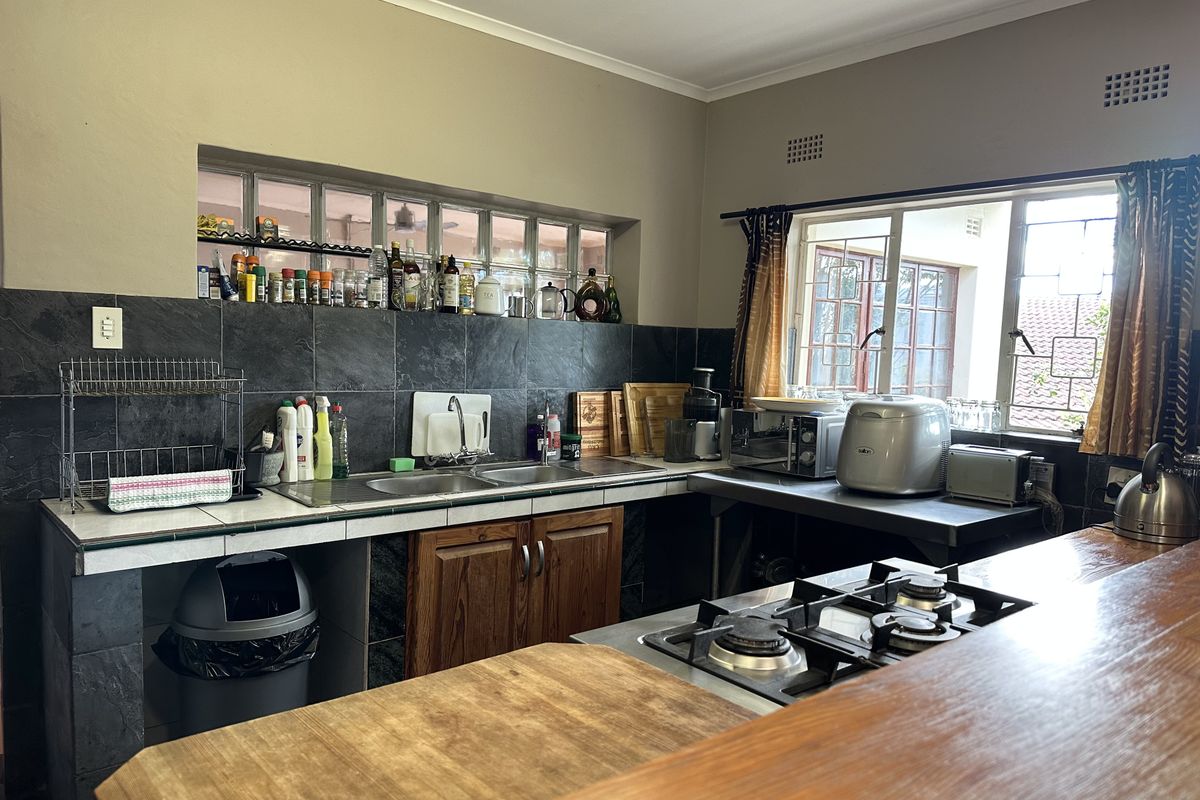 A functional kitchen featuring a gas hob, timber cabinetry, double bowl sink, and a breakfast bar with a tiled splashback and glass block window.