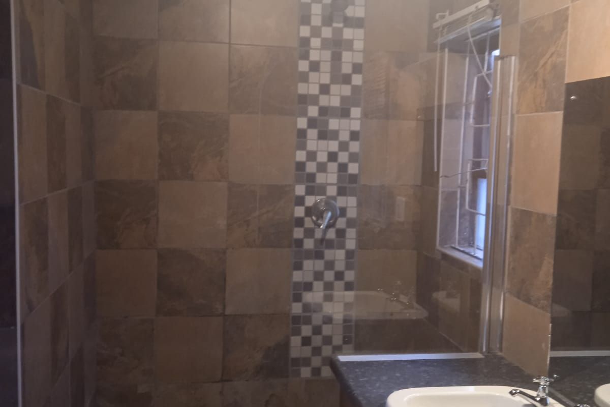 A bathroom featuring a shower with mosaic tile accents, a vanity cabinet with a basin, and tiled wall finishes.
