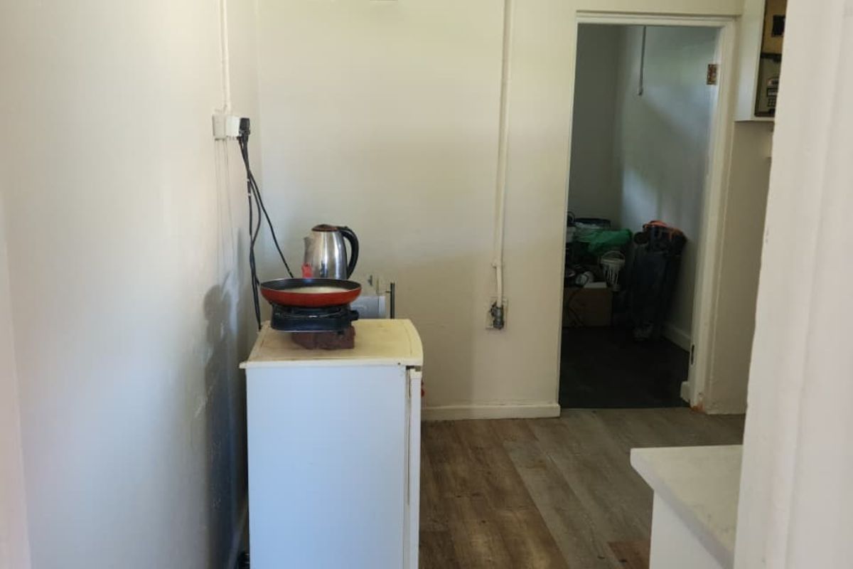 A basic utility space or kitchenette area featuring wood-look flooring and minimal fixed infrastructure, leading into an adjacent storage room.
