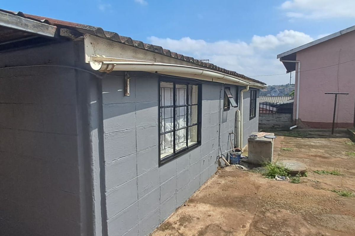 Rear exterior view of the property featuring concrete block walls, corrugated roofing, and security-barred windows with an adjacent yard area.
