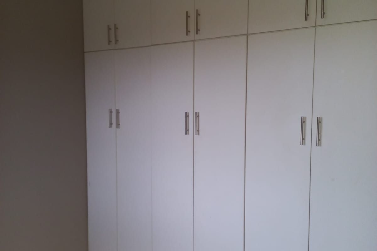 A bedroom featuring white built-in cupboards and neutral tiled flooring, providing ample storage space.