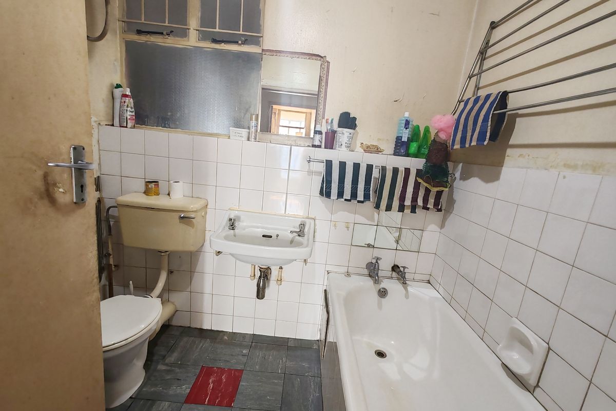 A dated bathroom featuring a standard bathtub, wall-mounted basin, and flush toilet with original tiled finishes, requiring modernization and refurbishment.