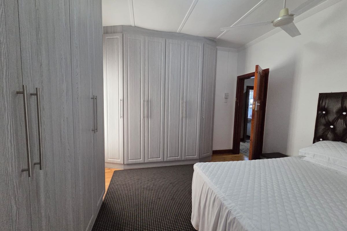 A bedroom featuring light-toned built-in wardrobes, timber flooring, and a ceiling fan, offering a clean and functional living space.