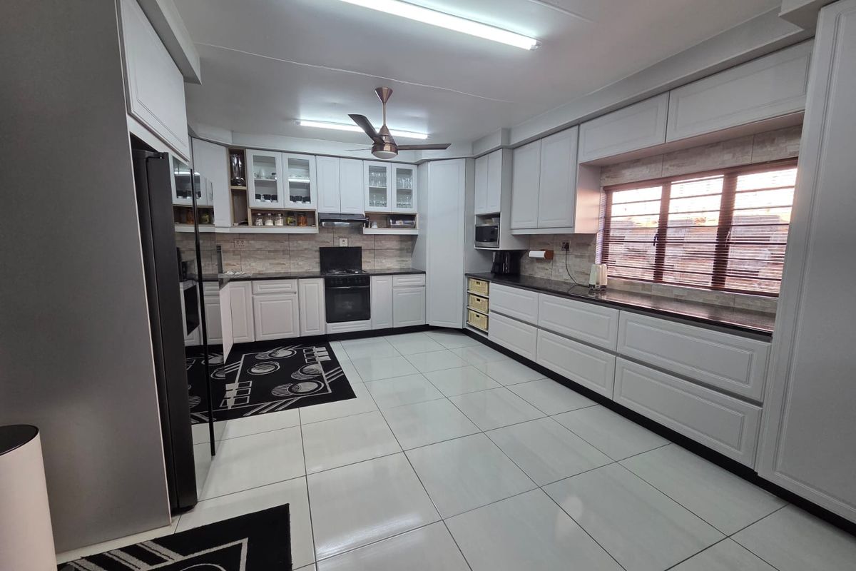 A spacious, well-maintained kitchen featuring extensive white cabinetry, dark granite countertops, built-in appliances, and large format floor tiles.