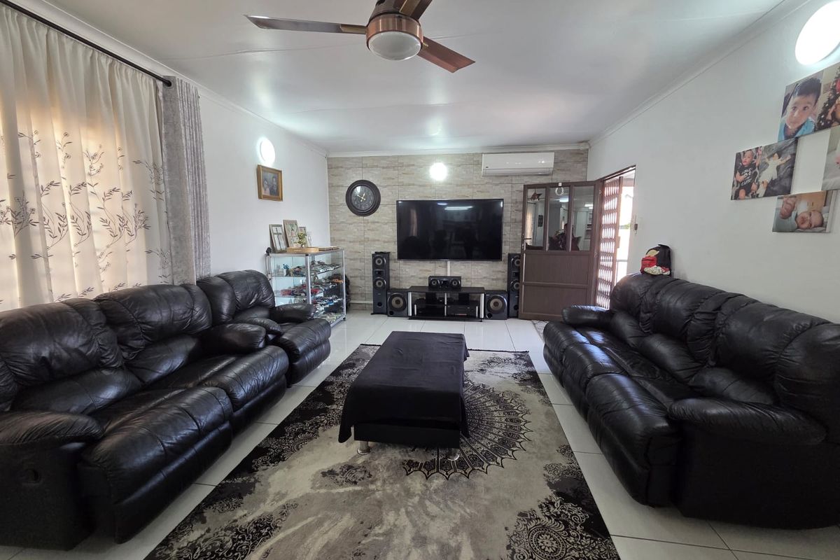 A spacious living room featuring a stone-cladding feature wall, tiled flooring, a ceiling fan, and a wall-mounted air conditioning unit.
