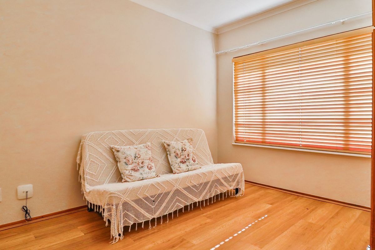 A bright bedroom featuring warm-toned laminate flooring, neutral walls, and fitted venetian blinds, offering a clean and comfortable living space.
