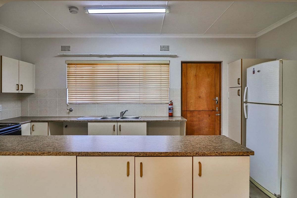 A functional kitchen featuring laminate countertops, double bowl sink, tiled splashback, and ample built-in cabinetry, offering a clean and practical workspace.