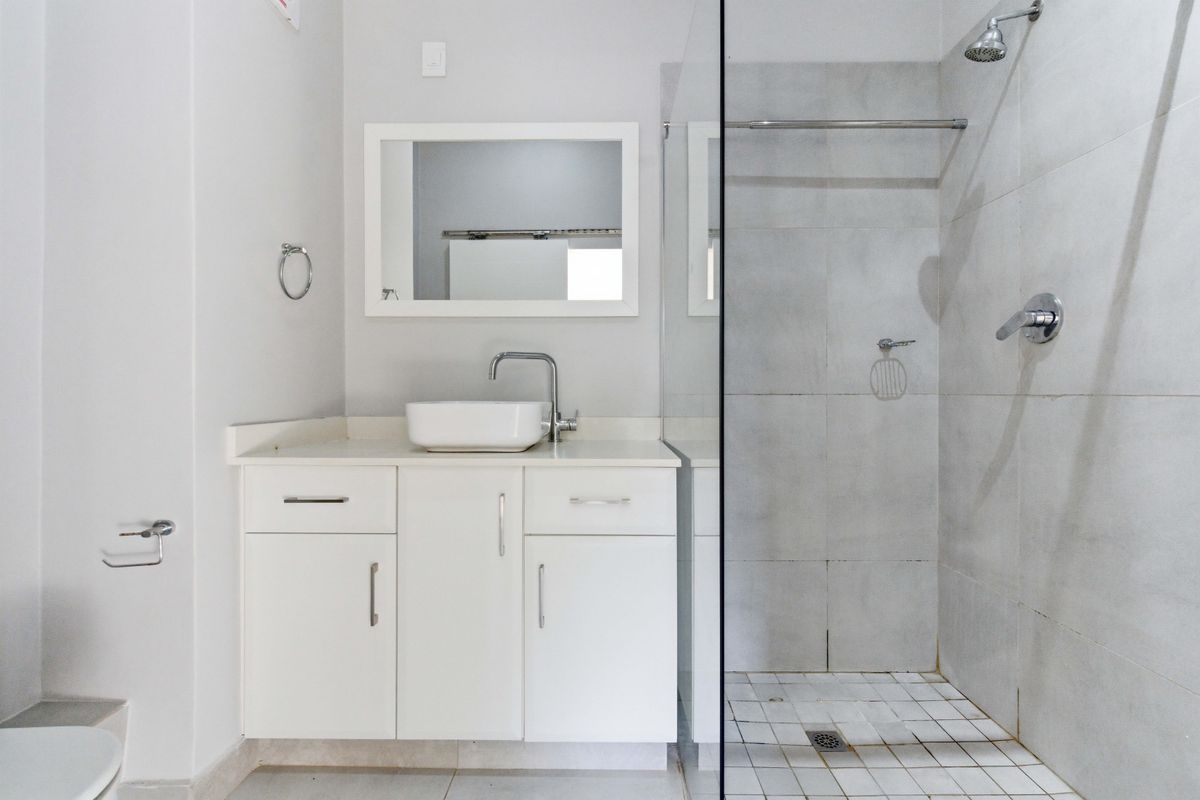 A clean, modern bathroom featuring a white vanity with a vessel sink, a glass-enclosed shower, and neutral wall tiling.