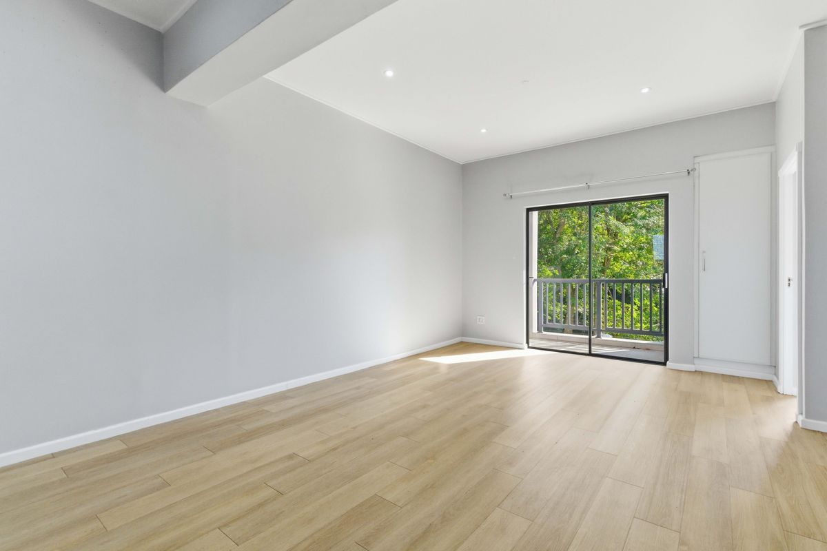 A bright, empty bedroom featuring modern laminate flooring, recessed lighting, and a sliding glass door leading to a private balcony.