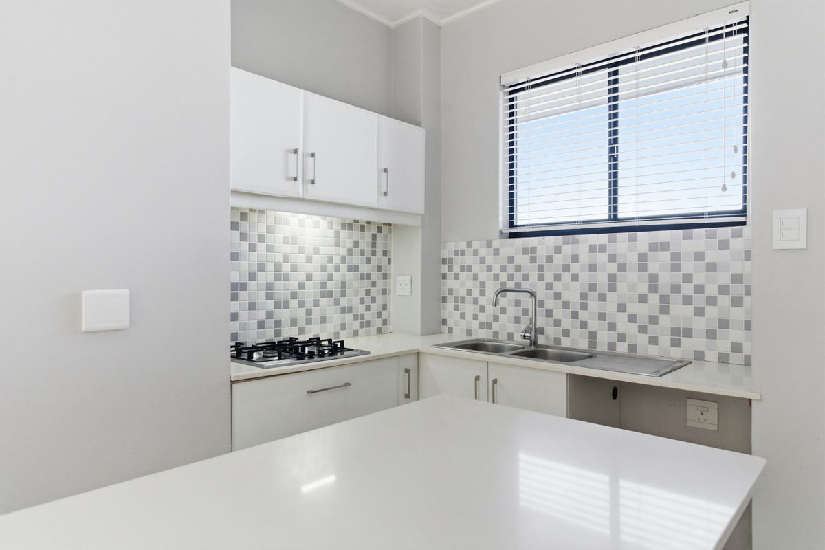 Modern kitchen featuring white cabinetry, stone countertops, a gas hob, and a mosaic tile backsplash with a functional double sink.