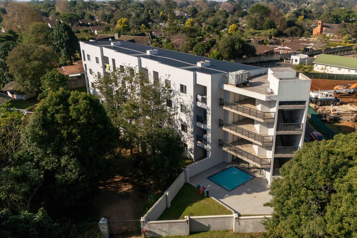 Aerial view of a multi-story apartment building featuring a swimming pool, private balconies, and rooftop solar panels set within a landscaped residential area.