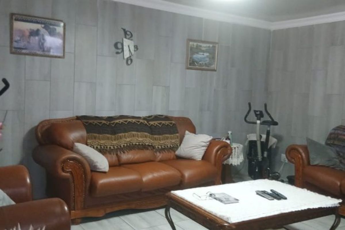 A living room featuring wood-look wall paneling, tiled flooring, and decorative coving, providing a neutral base for interior design updates.