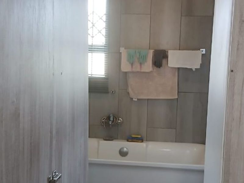 A bathroom featuring a bathtub with wall tiling and a window with security bars.