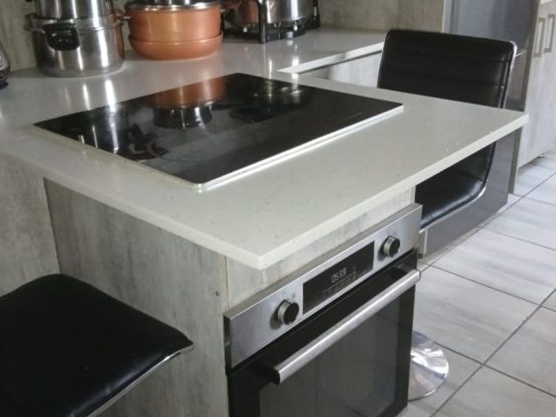 A modern kitchen island featuring a white quartz countertop, integrated electric induction hob, and a built-in oven with tiled flooring.