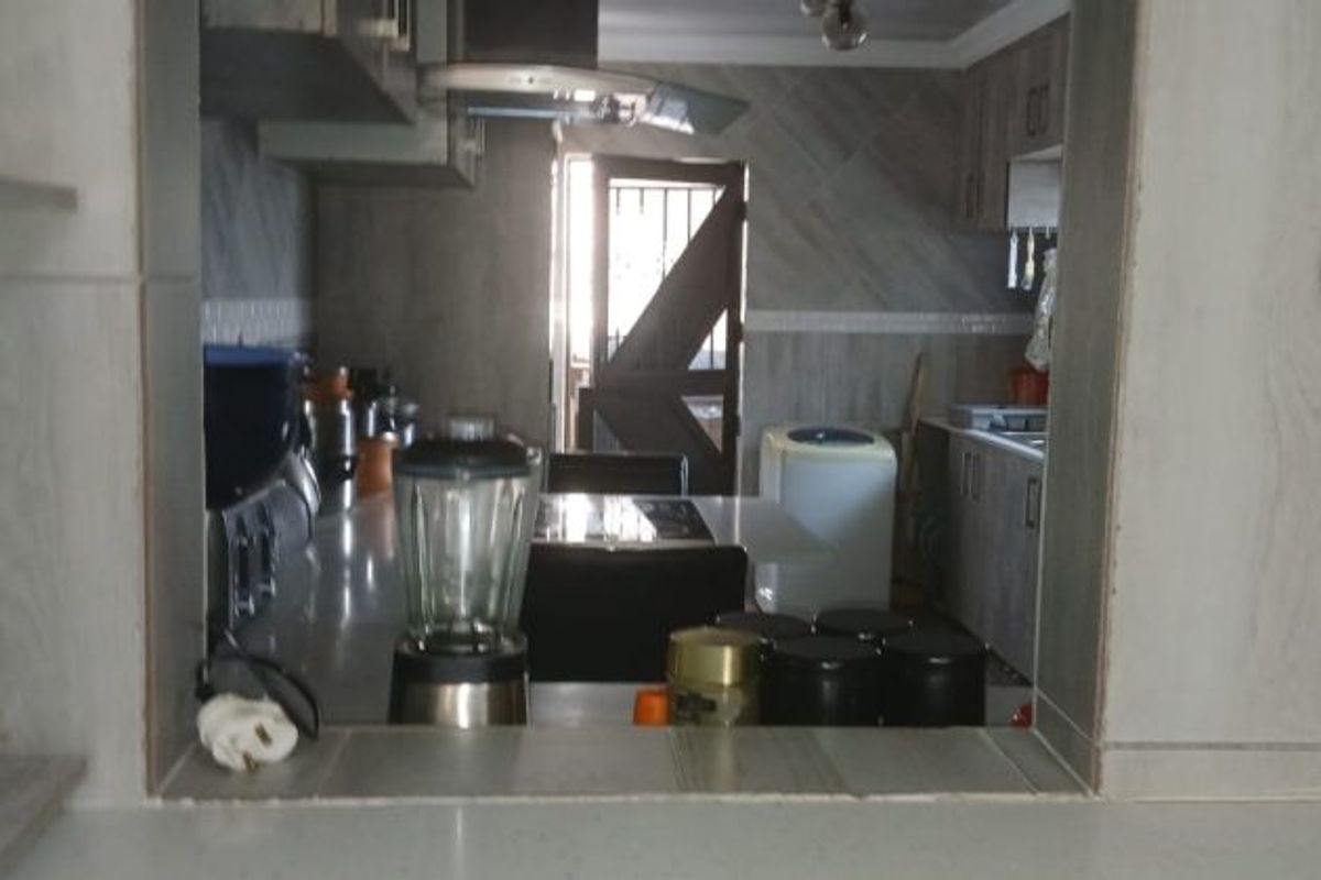A view through a serving hatch into a functional kitchen featuring built-in cabinetry, tiled finishes, and an extractor fan.
