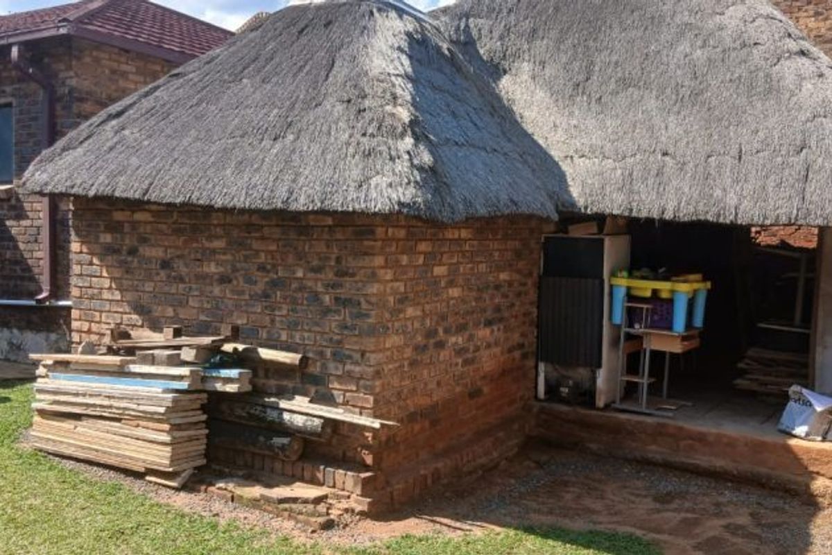 Rear view of a property featuring a traditional thatch roof structure and face brick exterior walls with an adjacent covered patio area.