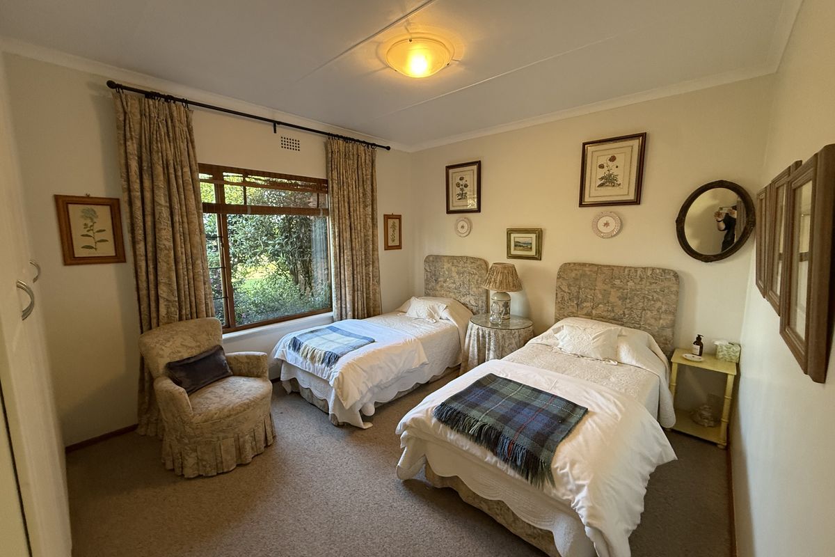 A well-lit bedroom featuring carpeted flooring, built-in cupboards, and a large window overlooking the garden.
