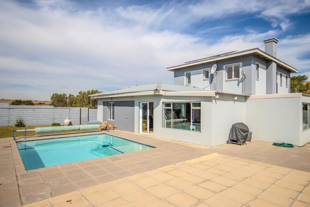 Rear view of the house featuring a swimming pool with a cover, paved patio area, and a multi-level exterior facade.