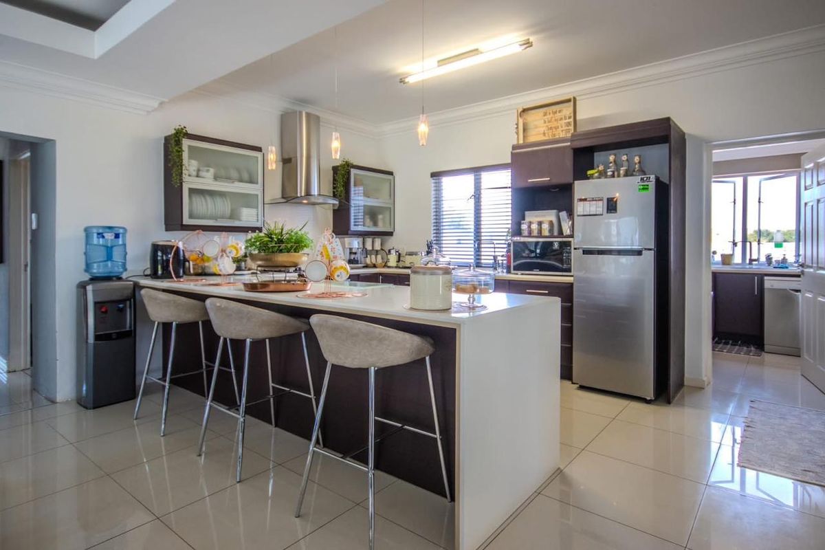 Modern open-plan kitchen featuring a central island with breakfast bar seating, dark cabinetry, stainless steel extractor fan, and tiled flooring.