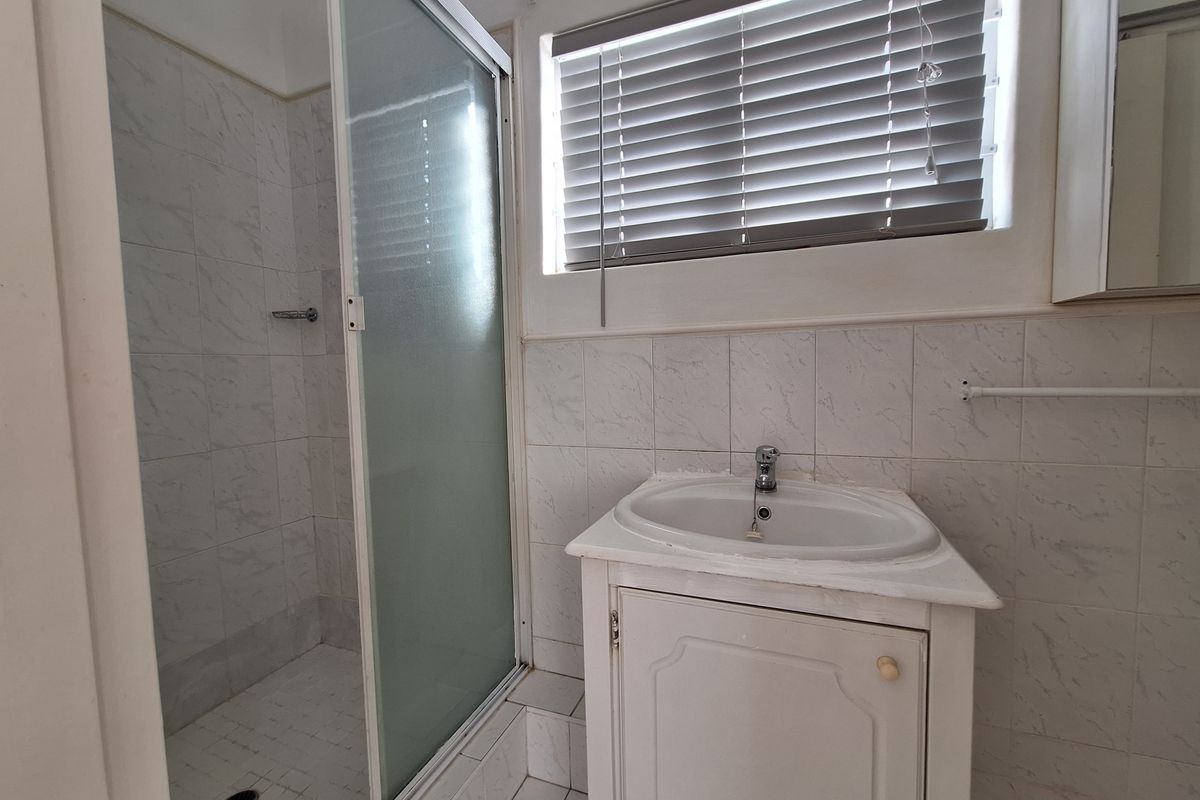 A functional bathroom featuring a glass-enclosed shower, a vanity basin, and tiled walls with a window for natural light.